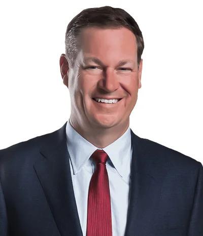 A man in a dark suit, white shirt, and red tie smiles at the camera against a plain white background.